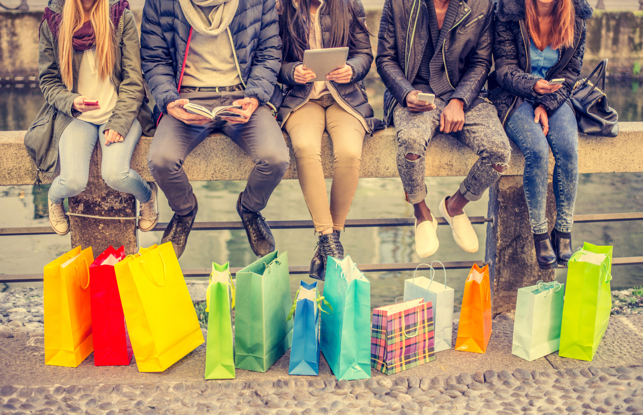 Eine Gruppe von fünf Personen sitzt draußen in der Stadt nebeneinander auf einem Geländer, vor ihnen stehen bunte Einkaufstaschen