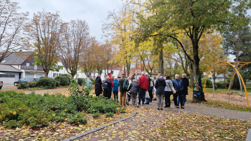 Menschengruppe im Park unter Bäumen neben einem Spielplatz. Stadtspaziergang mit Gewerbetreibenden im Rahmen vom Projekt "Griesheim. Innen Drin".