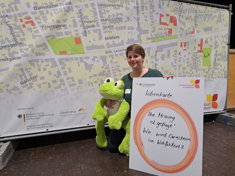 Theresa Lotichius, Geschäftsführerin der wer denkt was GmbH, bei einer Öffentlichkeitsveranstaltung zum Projekt "Griesheim. Innen Drin". Zu sehen ist eine Ideenkarte, ein Plakat mit Aufschrift "Ihre Meinung ist gefragt! Wie wird Griesheim ein Wohlfühlort?".