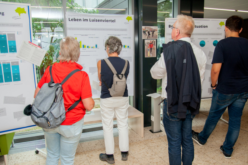 Abschlussveranstaltung zur crossmedialen Bürgerbeteiligung zum autofreien Laurentiusplatz in Wuppertal. 4 Personen stehen vor Infotafeln und können sich dort über die Ergebnisse der Bürgerbeteiligungsverfahren informieren.